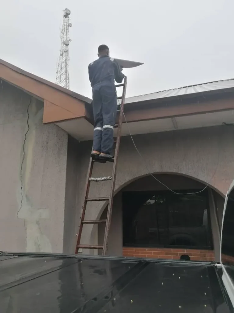 Installer on the ladder taking the Starlink dish up to the roof
