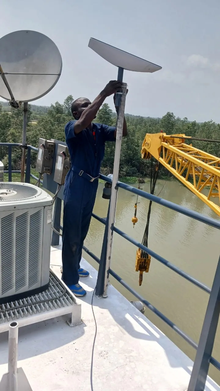 ZuraLink installer fixing a Starlink dish to a pole on a crane barge's deck railing over the river